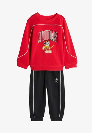 Crvena majica dugih rukava s natpisom "ADIDAS" i grafikom Mickey Mousea, u kombinaciji s crnim hlačama opremljenim bijelim detaljima i Adidas logom.