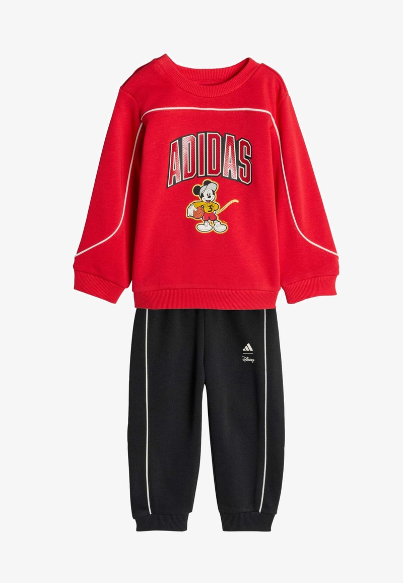 Crvena majica dugih rukava s natpisom "ADIDAS" i grafikom Mickey Mousea, u kombinaciji s crnim hlačama opremljenim bijelim detaljima i Adidas logom.