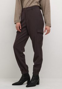 Pantalons cargo violet foncé avec une cheville élastique, des poches avant et une poche latérale, associés à des bottines à talons noires et un pull beige.
