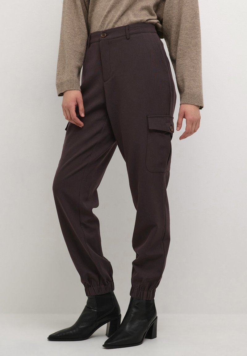 Pantalons cargo violet foncé avec une cheville élastique, des poches avant et une poche latérale, associés à des bottines à talons noires et un pull beige.