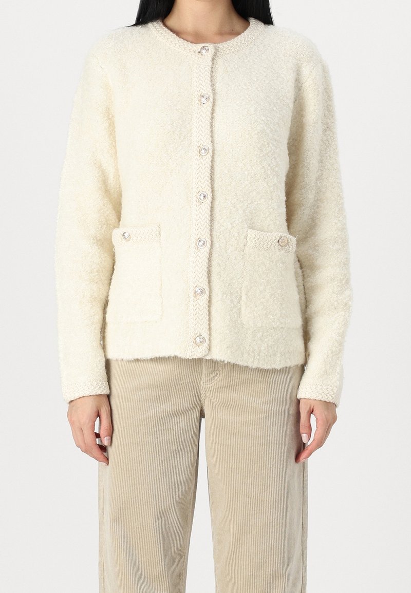 Krämfärgad cardigan i texturerat, fluffigt material; har rund hals, framknappar och två framfickor.