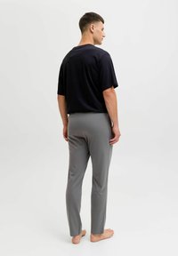 T-shirt nero a maniche corte da uomo e pantaloni grigi slim-fit. Tessuto morbido, design semplice e taglio rilassato. Piedi nudi visibili.