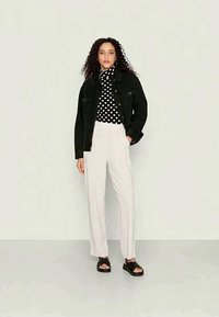 Veste en denim noire portée sur un haut à motifs en cœurs noir et blanc, associée à un pantalon léger et fluide de couleur claire et des sandales noires.