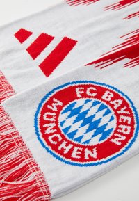 Šal FC Bayerna München, izrađen od pletene tkanine, bijele boje s crvenim akcentima i resama, s okruglim izvezenim logotipom koji sadrži plavi i bijeli dijamantni uzorak.