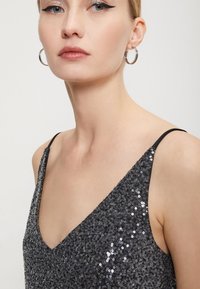 Strieborné flitrové šaty s výstrihom do V a tenkými čiernymi ramienkami, s textúrovaným povrchom a priliehavým strihom.