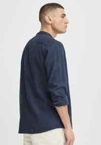 Camisa de manga larga azul marino en tejido texturizado con cuello, mangas enrollables y corte holgado, con un dobladillo recto y yugo trasero.