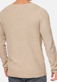 Beiger Strickpullover mit langen Ärmeln, Rundhalsausschnitt, strukturiertem Stoff und abgerundetem Saum, getragen zu grauen Hosen, Ansicht von hinten.