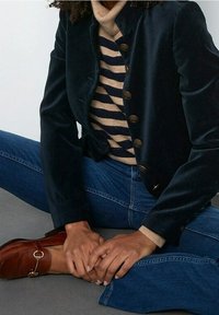 Námořnický sametový blejzr s vysokým límcem a pěti zlatými knoflíky, nošený přes béžový a námořnický pruhovaný rolák a modré džíny. Hnědá obuv.