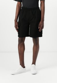 Sorte cargo shorts med elastisk talje, to sidelommer og to store cargo lommer. Bæres med hvide sneakers.