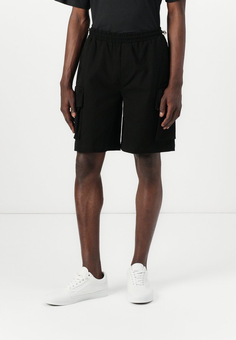 Sorte cargo shorts med elastisk talje, to sidelommer og to store cargo lommer. Bæres med hvide sneakers.