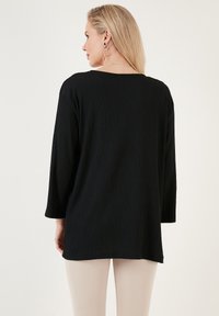 Haut à manches longues noir à côtes avec une coupe décontractée, ornée d'un large col et d'un ourlet légèrement arrondi, associée à un pantalon de couleur claire.