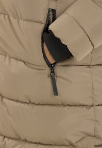 Beige pufferjakke med en quiltet design, med en lynlåslomme og en sort elastisk manchet ved ærmet. Glat, skinnende overflade.