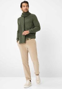 Maglione verde a coste in lana con sciarpa coordinata, pantaloni in corduroy beige e sneakers crema. Dettagli semplici e testurizzati in un outfit casual.