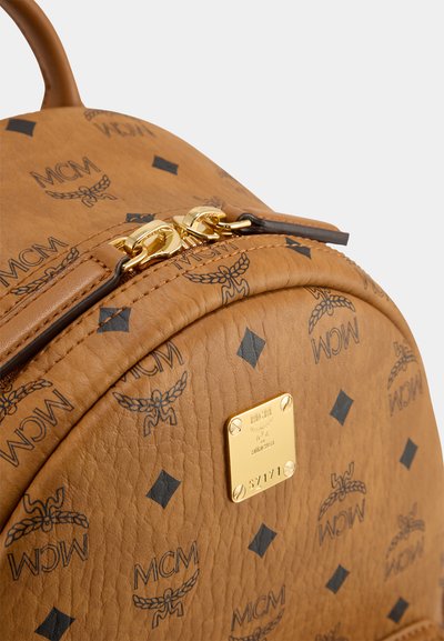 Sac à dos en cuir tan avec motif logo MCM noir. Présente une fermeture éclair et des accessoires en or. Forme arrondie avec des accents cousus. Plaque logo métallique.