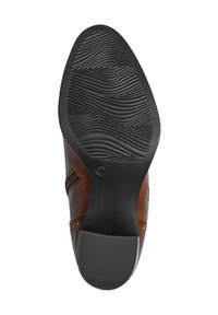 Chaussure en cuir marron avec une semelle en caoutchouc noir texturé, présentant des motifs en vagues et un bout arrondi, accentuée par de petites rivets métalliques sur le côté.