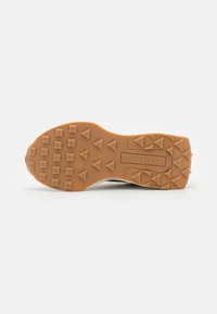 Sole di scarpa sportiva realizzata in materiale gommoso marrone, con suole a forma di triangolo per una migliore aderenza e marchiatura in rilievo al centro.