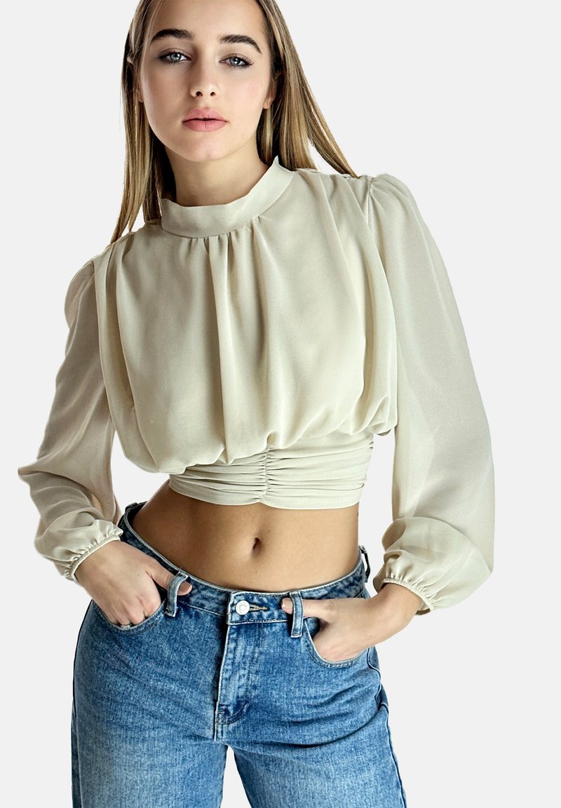 Bluzka w kolorze kremowym, lekka, z bufkami i zebranym stanem, zestawiona z dżinsami w kolorze niebieskim o wysokim stanie. Gładka tekstura, casualowy design.