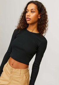Zwarte geribbelde crop top met lange mouwen, zachte textuur, ronde halslijn, gecombineerd met hooggesneden beige broeken. Minimalistisch ontwerp.