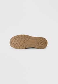 Suela de goma con un patrón de relieve en forma de panal en marrón claro. Presenta un logotipo y acentos texturizados para un mejor agarre.
