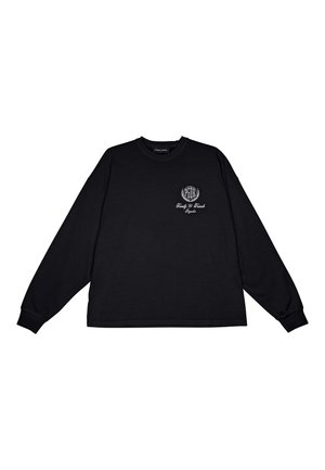 Sweatshirt noir à manches longues avec un col rond, présentant un petit emblème blanc sur la poitrine gauche et des poignets côtelés. Texture de tissu lisse.