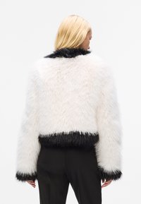 White faux fur cropped jacket with black trim on the cuffs and hem. Features a soft, fluffy texture and a high collar.