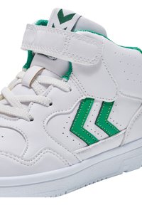 Białe sneakersy za kostkę z zielonymi akcentami w kształcie chevronu, perforowanymi detalami i rzepem nad sznurówkami. Teksturowana gumowa podeszwa.