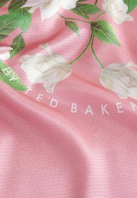Floral-patterned textile in pink with white flowers and green leaves, featuring the text "by Ted Baker" in white. Soft, textured appearance.