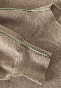 Hnedá pletená látka so zeleným doplnkovým prešívaním, vyznačujúca sa jemnou textúrou a rebrovaným dizajnom. Tvar zdôrazňuje závesný, vrstvený vzhľad.