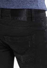 Jeans in denim nero con vestibilità slim, caratterizzati da una tasca posteriore visibile, tessuto testurizzato e una patch con logo in pelle sulla cintura.