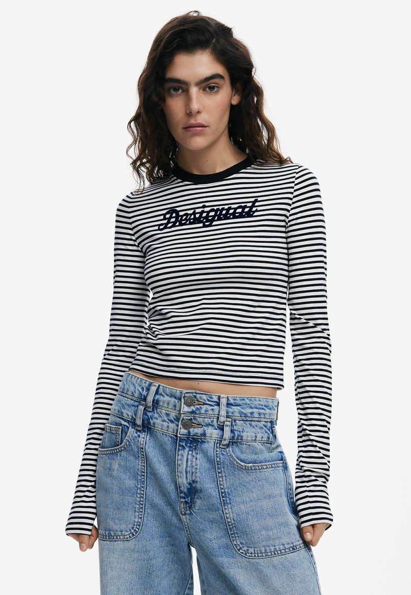 Čierno-bielo pruhovaný dlhý rukáv top s crop strihom, na ktorom je modrý nápis "Desigual". Nosí sa s svetlomodrými džínsami s vysokým pásom.