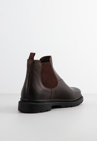 Stivaletti in pelle marrone con pannelli laterali elastici, dettagli in tessuto testurizzato, linguetta e una suola in gomma nera. Finitura liscia.