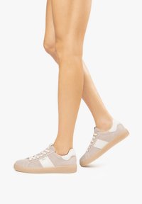 Beige sneakers with white accents, textured suede material, round toe, flat rubber sole, and lace-up closure.