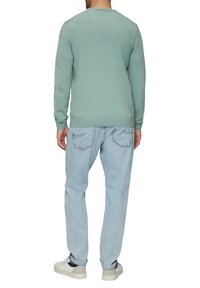 Hellgrüner Pullover mit Rundhalsausschnitt und gerippten Bündchen, kombiniert mit hellblauen Jeans. Das Material wirkt weich und strukturiert.