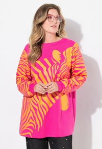 Felpa rosa brillante con grandi strisce di zebra gialle, maniche lunghe e taglio rilassato. Tessuto testurizzato con polsini a costine.