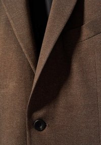 Blazer marron à chevrons avec revers cranté, un bouton noir unique et poche poitrine passepoilée, présenté en gros plan.