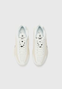 Paire de baskets blanches Nike Shox vues de dessus sur un fond clair uni, montrant les lacets et les étiquettes de languette brandées.