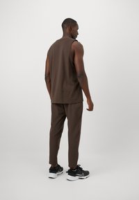 Chemise sans manches marron et pantalon ajusté marron assorti, accompagnés de chaussures de sport noires. Le tissu semble lisse et mat.