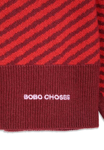 Tissu tricoté avec des rayures diagonales rouges et rouge foncé et un ourlet côtelé brodé de "BOBO CHOSES" en fil blanc.