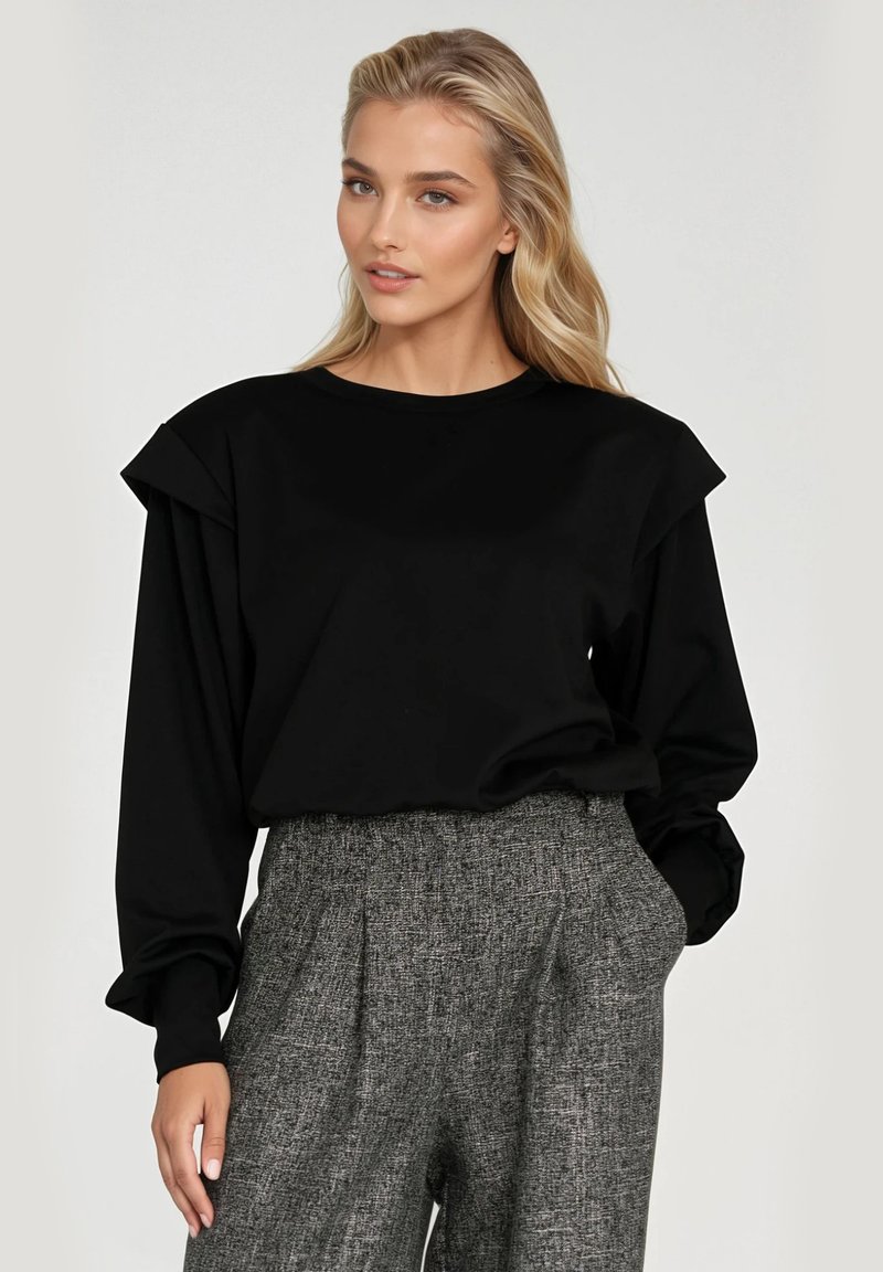 Czarny długi rękaw top z wyraźnymi falbanami na ramionach, okrągły dekolt, gładka tekstura. Połączony z jasnoszarymi spodniami z tweedu o wysokim stanie.