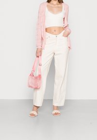Světlý růžový cardigan, bílý cropped top a béžové široké kalhoty. Průhledná růžová taška a smetanové pletené sandály dokončují vzhled.