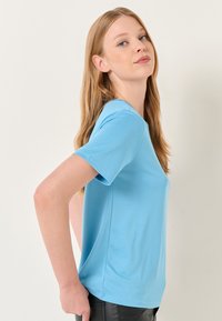 Lichtblauw t-shirt met korte mouwen van gladde stof, met een relaxte pasvorm en een ronde halslijn, gecombineerd met donkere broeken.