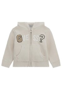 Veste à capuche zippée beige en tricot avec le mot "GUESS" dans des textures variées, deux poches avant et une finition douce et texturée.