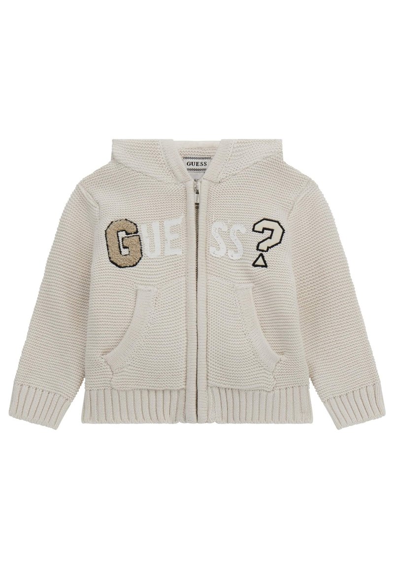 Veste à capuche zippée beige en tricot avec le mot "GUESS" dans des textures variées, deux poches avant et une finition douce et texturée.