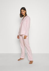 Rosa rutigt pyjamas-set med långa ärmar och byxor, tillverkat av mjukt tyg med avslappnad passform. Anmärkningsvärt knapplist med krage.
