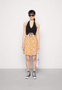 Top cropped preto com detalhes franzidos, saia floral amarela e rosa, sapatilhas altas pretas e uma bolsa lilás clara.