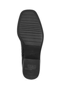 Suela de zapato negra con goma texturizada, con ranuras horizontales para un mejor agarre y un logo elevado. Bordes suaves con un diseño de punta redondeada.