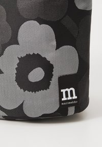 Black fabric bag featuring large gray floral patterns and a white "m" logo tag. The texture is smooth with a subtle sheen.