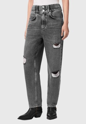 Kvinders grå high-waist jeans med slidte detaljer, elastisk linning, to frontknapper og sorte ankelstøvler på en lys baggrund.