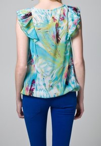 Blouse à motif floral, à manches courtes avec des accents volants ; principalement bleue avec des nuances de vert, rose et violet ; tissu léger.
