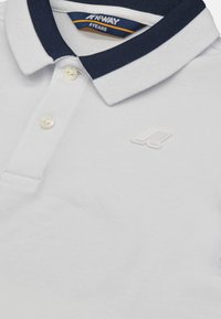 Polo bianca in cotone, con colletto navy a strisce bianche, tre bottoni e un sottile logo bianco sul petto.